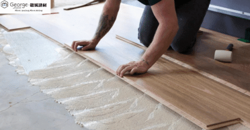 A worker is installing engineered timber flooring, with adhesive spread on the floor